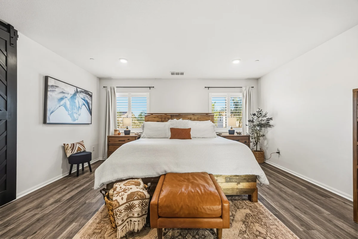 Bedroom with a white bed, leather bench and framed artwork