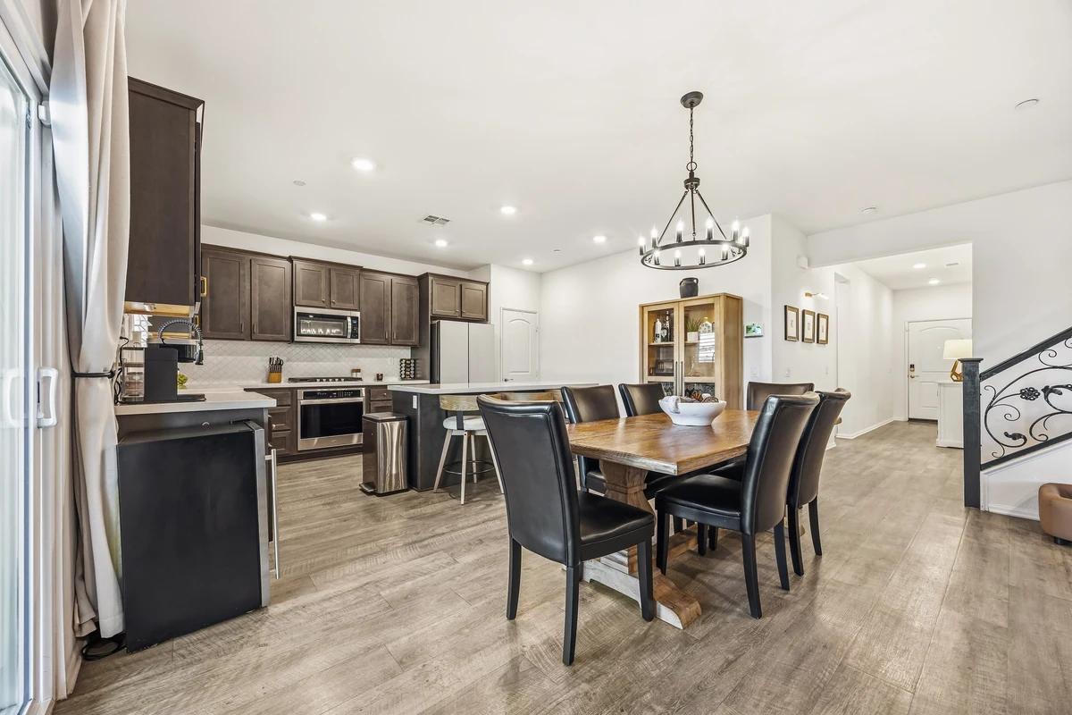Dining table with black chairs beside a kitchen with dark cabinets
