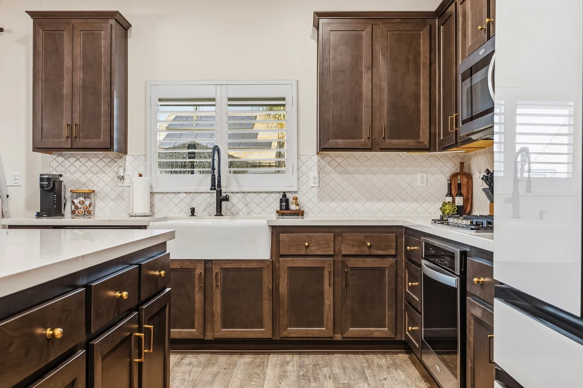 Kitchen sink below a shuttered window between dark wood cabinets