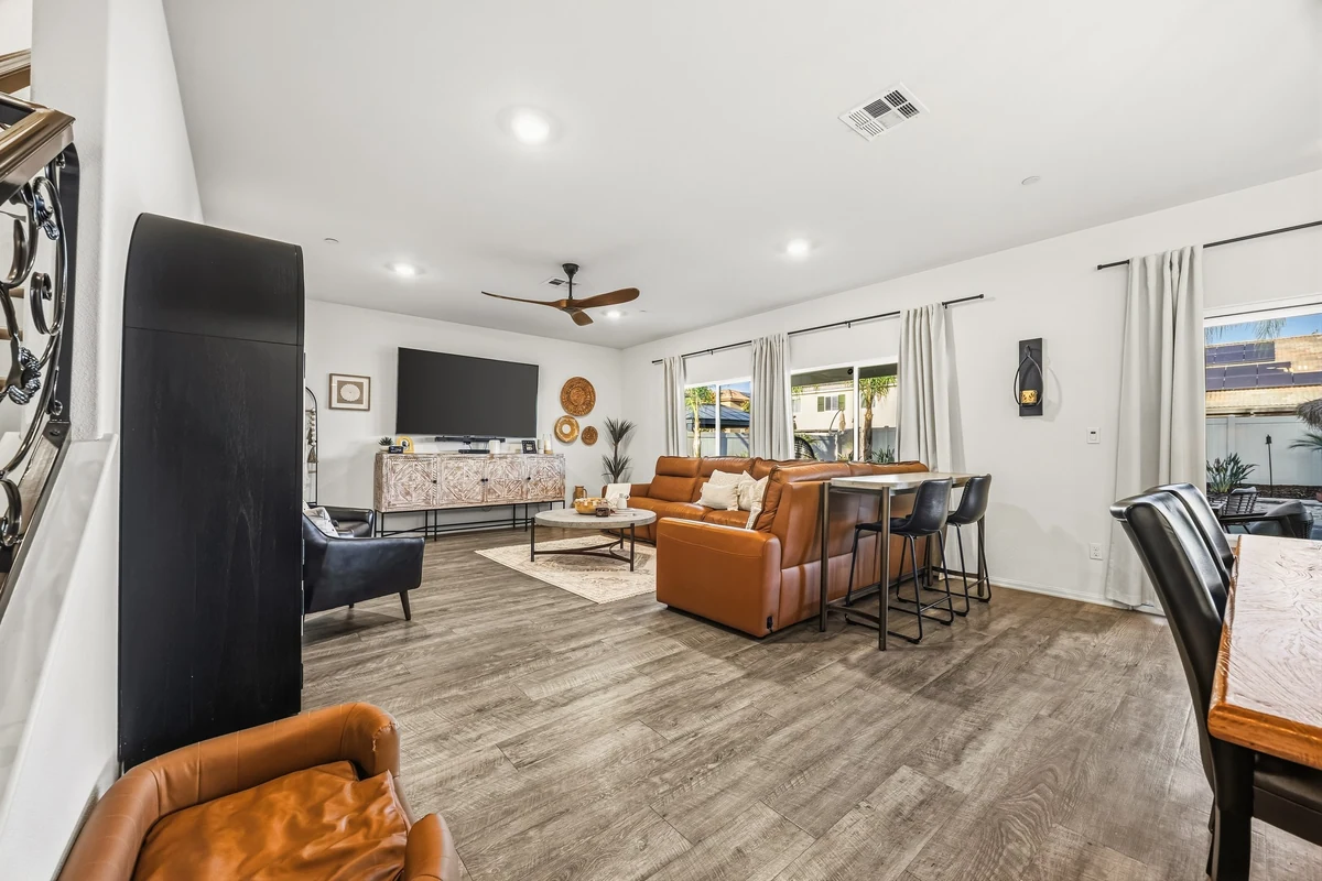 Open living room with brown leather seating, a ceiling fan and sliding patio doors
