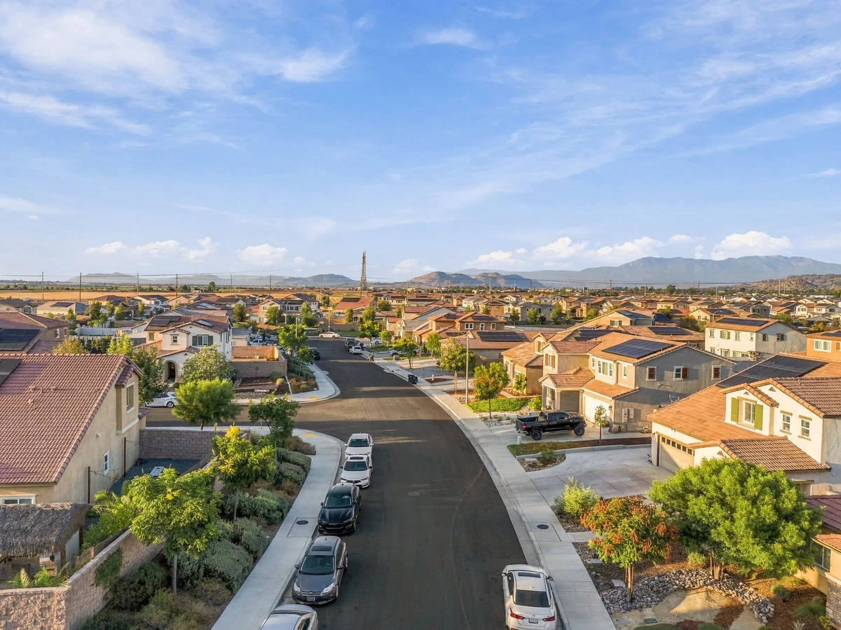 Aerial view along a residential street with tiled-roof homes and distant hills