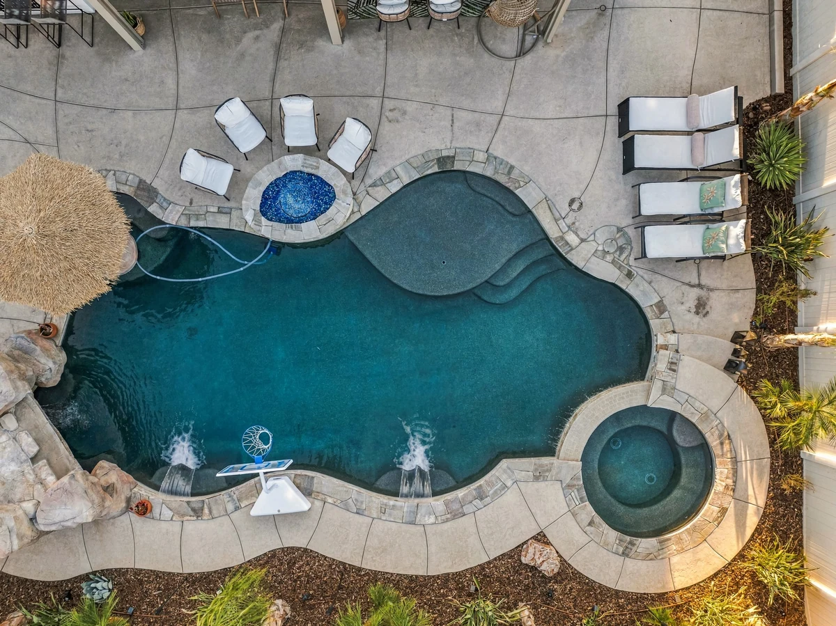 Overhead view of a curved swimming pool, circular spa and poolside loungers