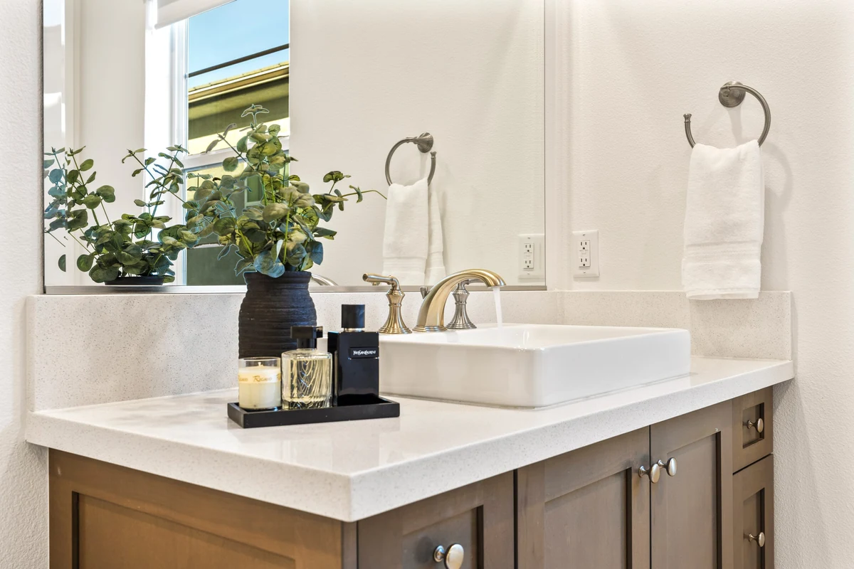 Bathroom vanity with a vessel sink, gold faucet and a vase of greenery