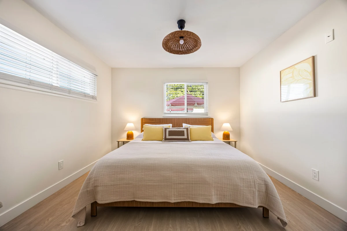 Bed beneath a woven pendant light with windows on two walls