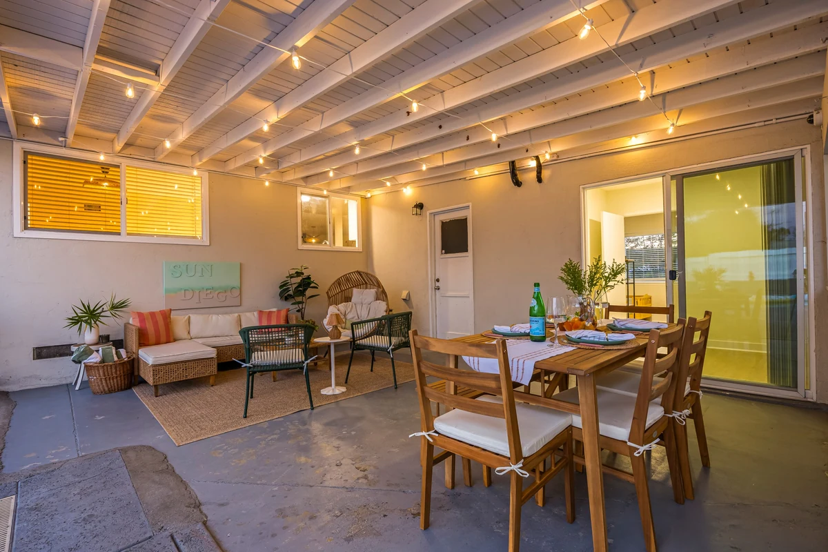 Covered patio with exposed beams, string lights, dining table and seating