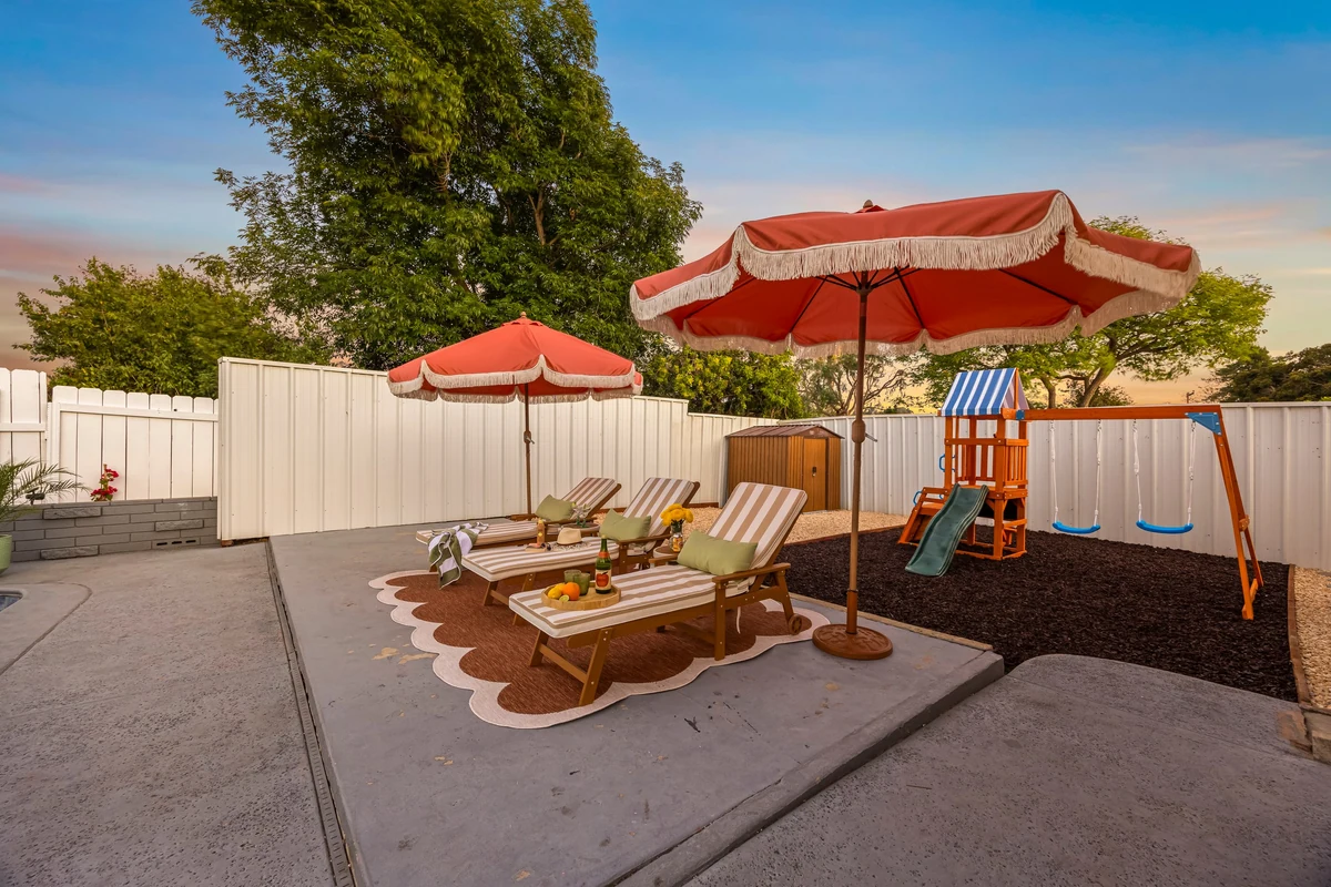Wooden loungers beneath red umbrellas beside a backyard play area